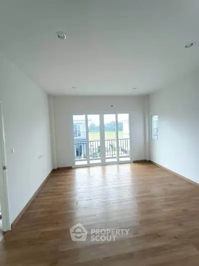 Spacious empty room with wooden flooring and large windows offering natural light.