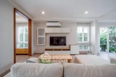 Spacious modern living room with natural light and garden view, featuring cozy seating and sleek entertainment center.