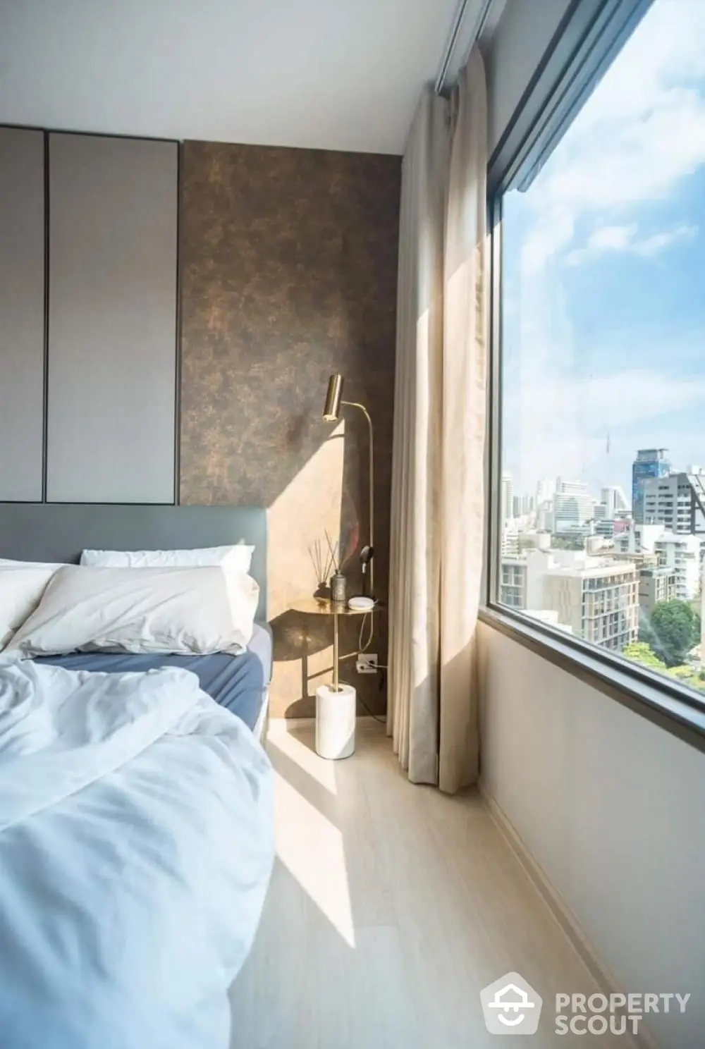 Modern bedroom with large window offering stunning city view, elegant decor, and cozy atmosphere.