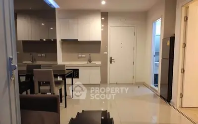 Modern apartment interior with sleek kitchen and dining area, featuring glossy cabinets and tiled flooring.