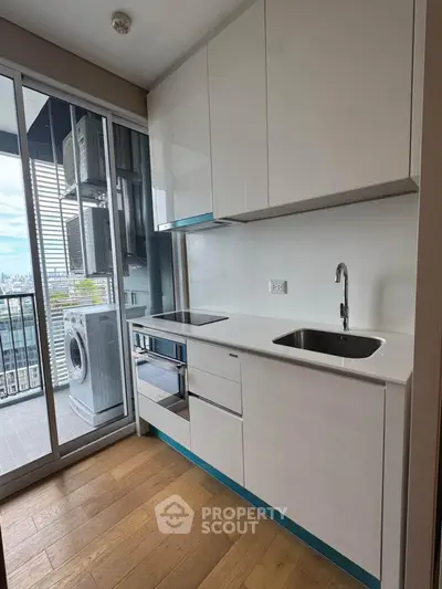 Modern kitchen with sleek cabinetry and balcony view, featuring a washing machine and city skyline.