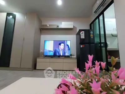 Modern living room with sleek furniture and kitchen view, featuring a flat-screen TV and stylish decor.