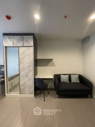 Modern minimalist living room with sleek furniture and ample lighting, featuring a cozy sofa and a practical study area with a view.
