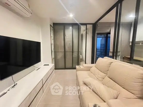 Modern living room with beige sofa, large TV, and glass sliding doors leading to balcony.