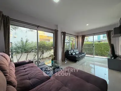 Spacious living room with large windows and garden view, featuring modern sofas and sleek flooring.