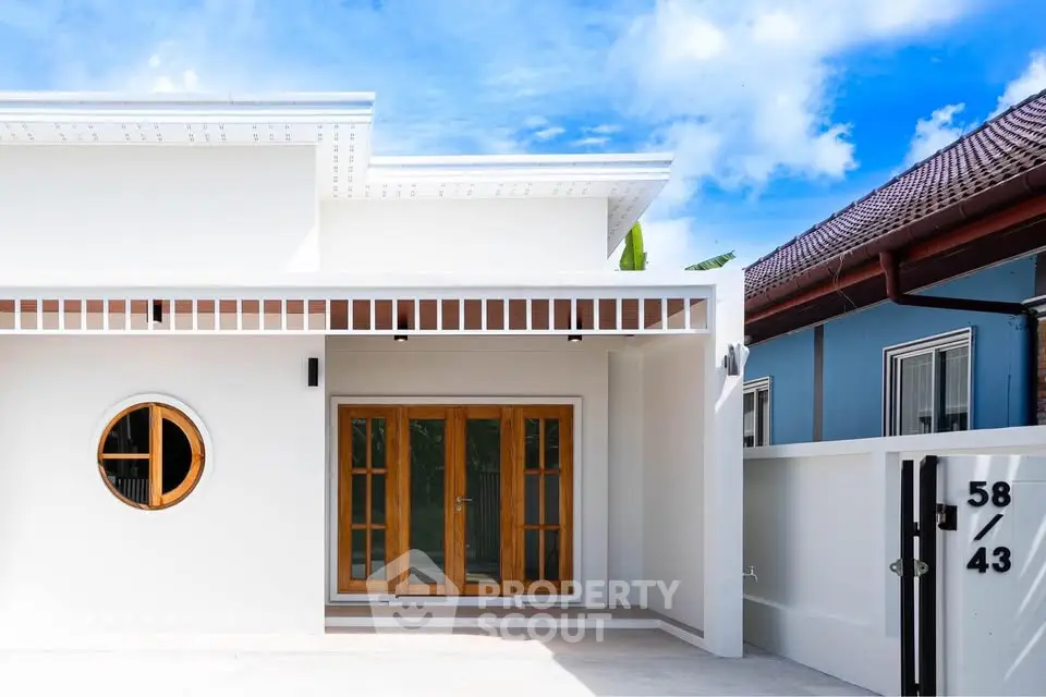 Modern white house exterior with wooden doors and circular window, showcasing minimalist architecture under a clear blue sky.