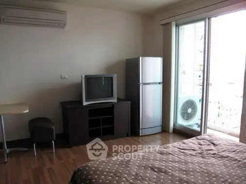 Cozy bedroom with balcony access, featuring a TV and fridge, ideal for modern living.