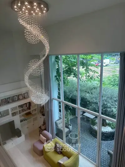 Luxurious living room with high ceiling, elegant chandelier, and large windows overlooking a lush garden.