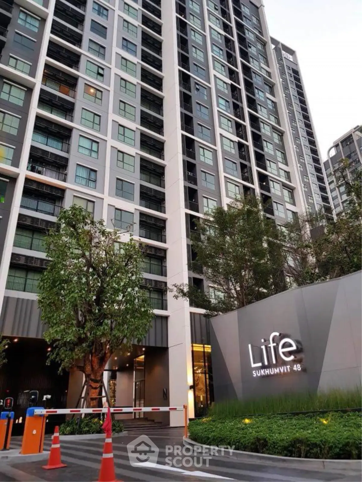 Modern high-rise condominium building with sleek design and lush landscaping in urban setting.