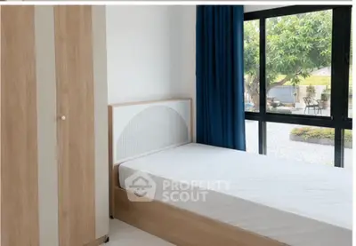 Bright bedroom with large window and garden view, featuring minimalist wooden furniture.