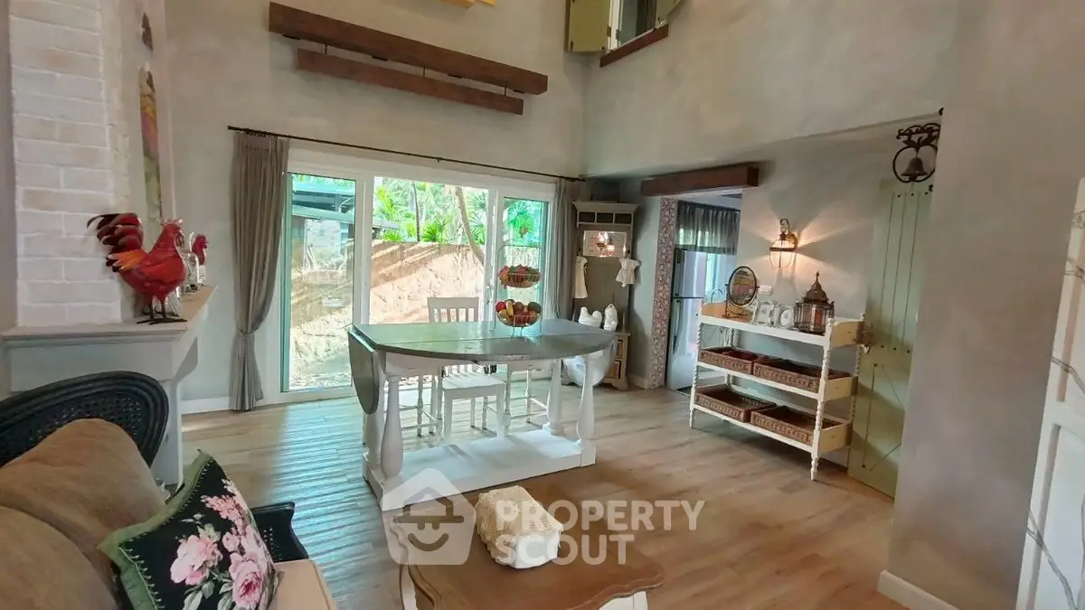Charming rustic living room with wooden floors, cozy decor, and large windows overlooking lush greenery.