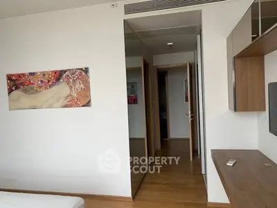 Modern bedroom with wooden flooring and stylish wall art, featuring sleek built-in furniture.