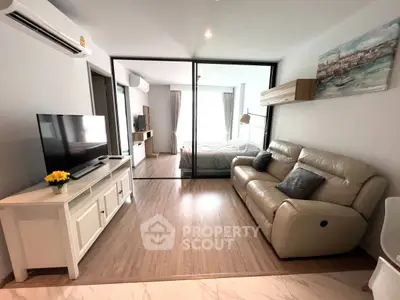 Modern living room with cozy leather sofa and large TV, open to a bright bedroom.