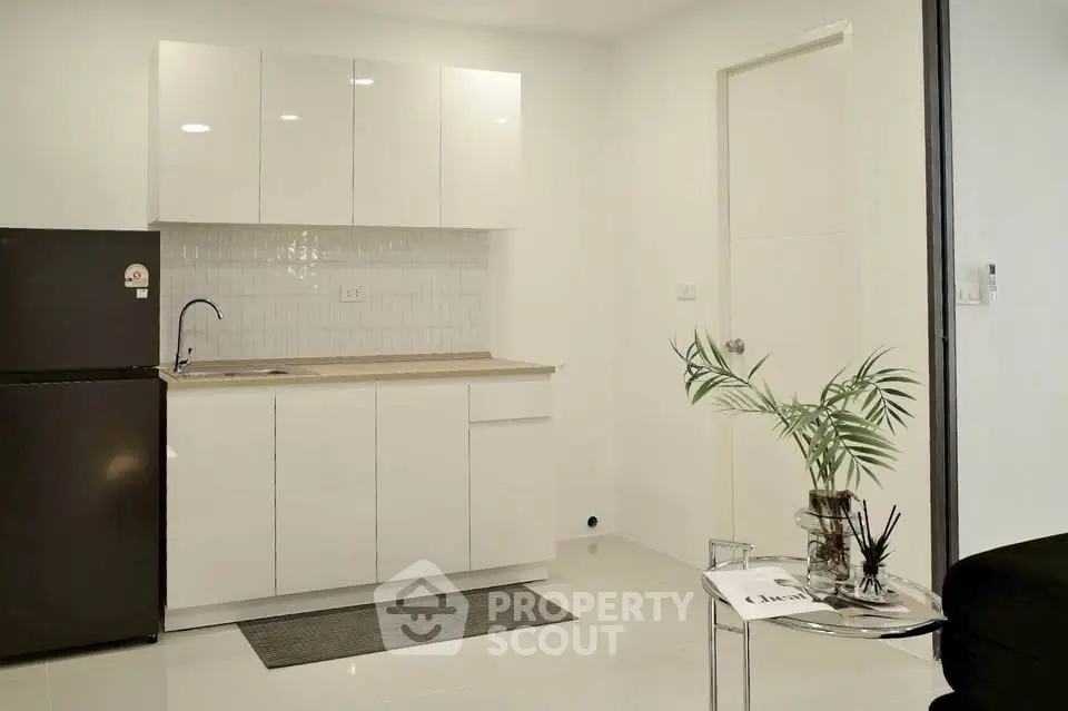 Modern minimalist kitchen with sleek white cabinets and compact fridge