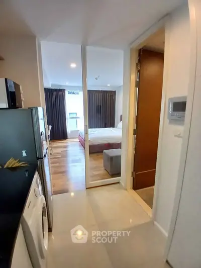 Modern apartment hallway leading to a cozy bedroom with wooden flooring and natural light.