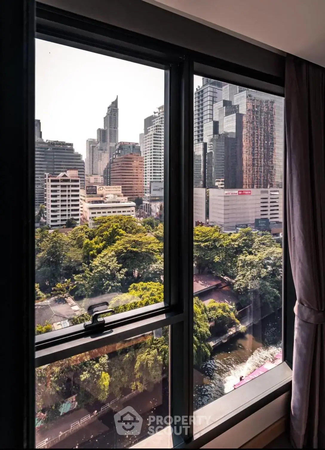 Stunning cityscape view from a high-rise apartment window overlooking lush greenery and skyscrapers.