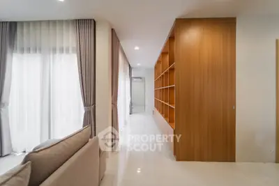 Modern living room with elegant curtains and built-in wooden shelving, featuring a cozy sofa and glossy white flooring.