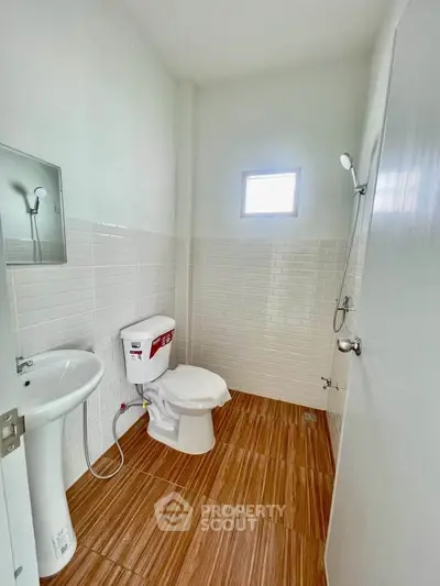 Modern bathroom with white tiles and wooden floor, featuring a shower and toilet.
