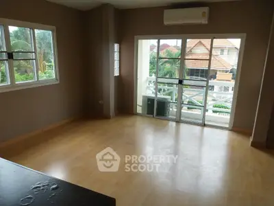 Spacious empty living room with wooden flooring and large windows offering natural light and garden view.