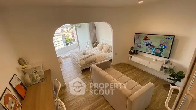 Modern living room with cozy seating and large TV, featuring a bright bedroom view through an archway.