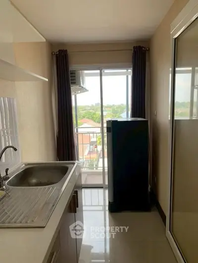 Compact kitchen with sink and fridge, offering a bright view through large window.