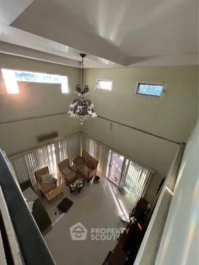 Spacious living room with high ceiling and elegant chandelier, featuring large windows and cozy seating area.