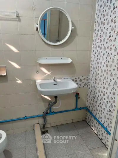 Compact bathroom with round mirror, wall-mounted sink, and vintage tile accents.