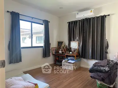 Cozy bedroom with wooden flooring and air conditioning, featuring a window with curtains and a comfortable sleeping area.