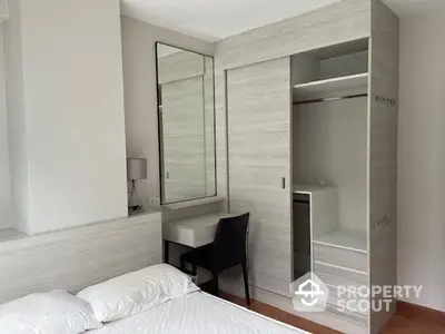 Elegant bedroom with built-in wardrobe and large mirror, showcasing a minimalist design with neutral tones and ample natural light.