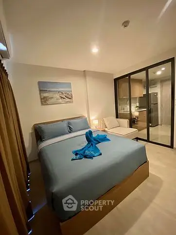 Cozy modern bedroom with blue bedding and glass partition to kitchen area.
