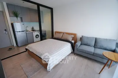 Modern studio apartment with cozy bedroom and compact kitchen featuring washing machine and fridge.