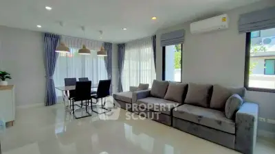 Modern living room with plush gray sofa and dining area, featuring large windows and stylish lighting.