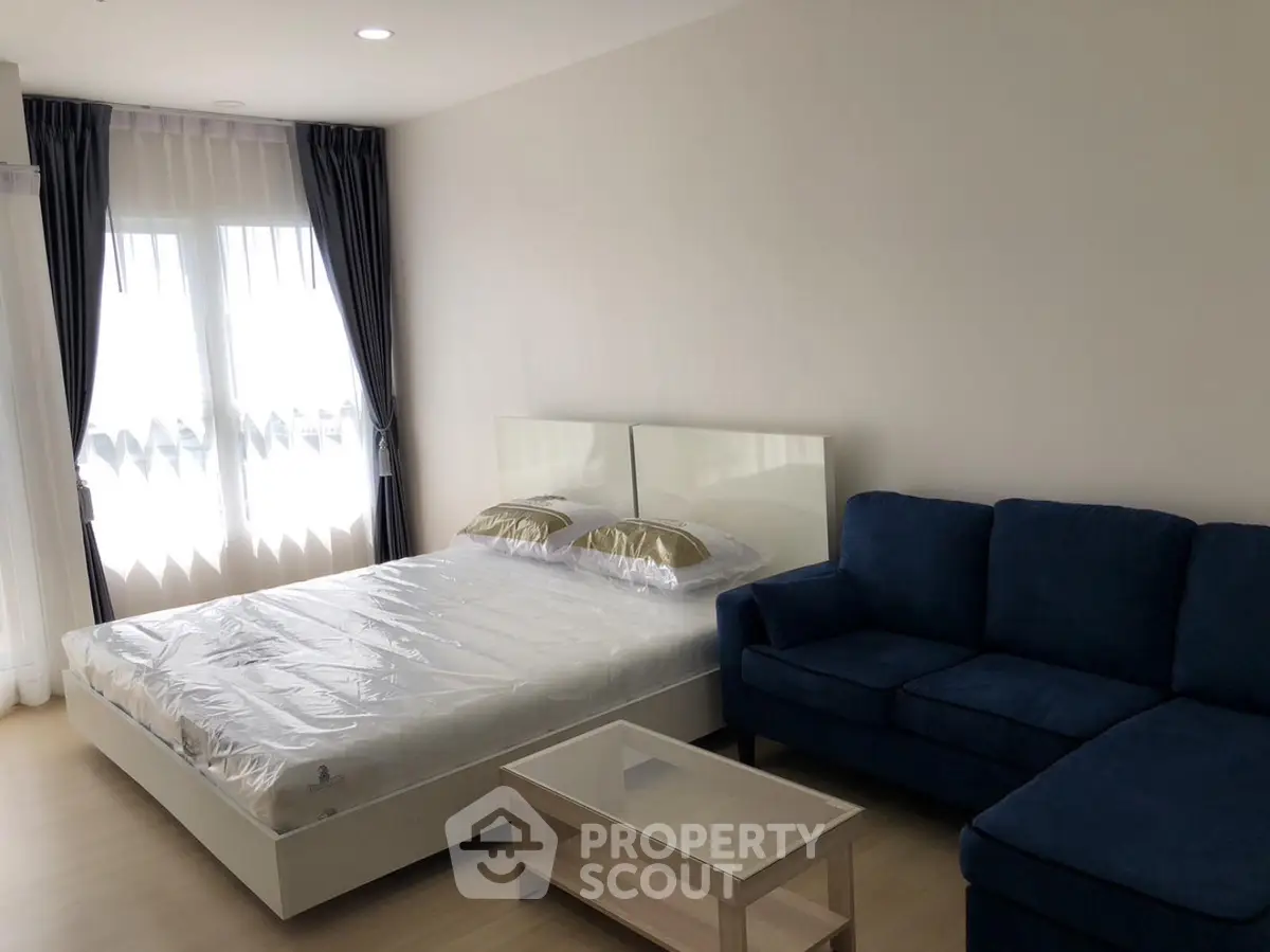 Modern bedroom with cozy blue sofa and natural light from large windows.