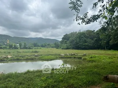 Scenic view of lush green landscape with hills and pond, perfect for serene real estate development.