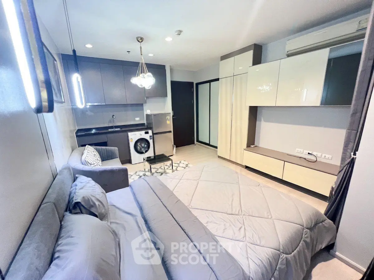 Modern studio apartment with sleek kitchen and cozy living area, featuring a washing machine and stylish lighting.