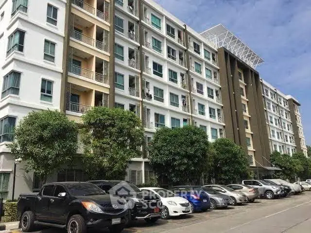 Modern apartment building with parking area and lush greenery, ideal for urban living.