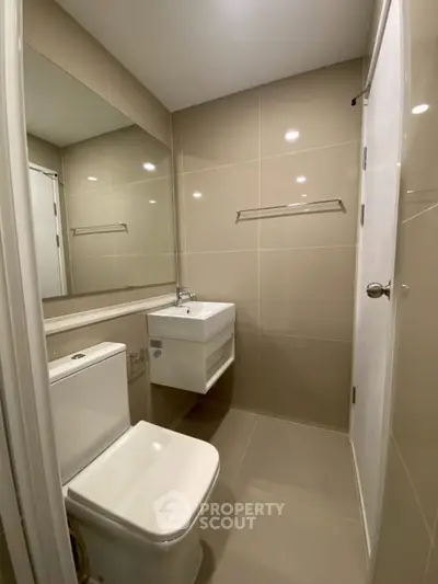 Modern bathroom with sleek fixtures and neutral tiles, featuring a wall-mounted sink and large mirror.