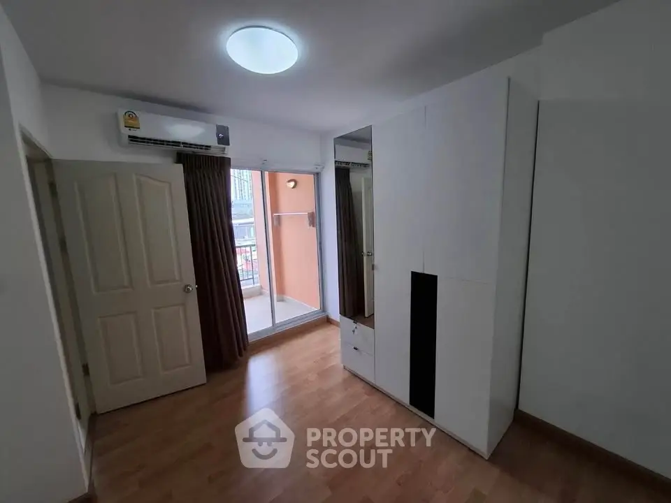 Spacious bedroom with wooden flooring and balcony access in modern apartment.