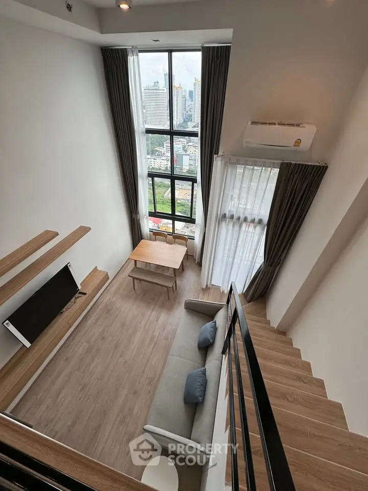 Modern loft apartment with high ceilings and large windows offering city views, featuring a cozy living area and stylish decor.