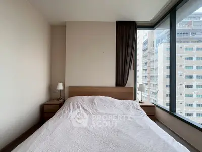 Modern bedroom with large windows offering city views, featuring a cozy bed and minimalist decor.