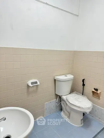 Simple bathroom with beige tiles and blue floor, featuring a toilet and sink.