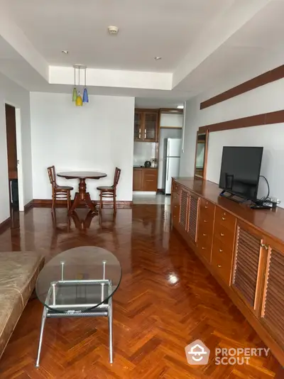 Spacious living room with polished hardwood floors, leading to an open layout kitchen with wooden cabinets and modern appliances.