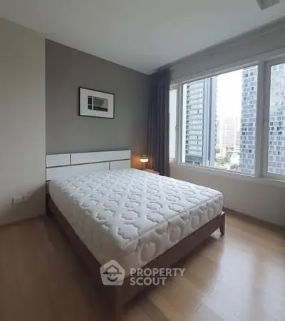 Modern bedroom with city view, featuring a comfortable bed and large windows for natural light.