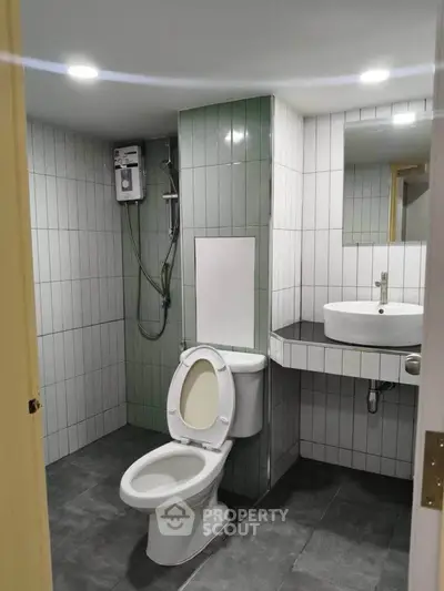 Modern bathroom with sleek design, featuring a toilet, sink, and shower area with water heater.