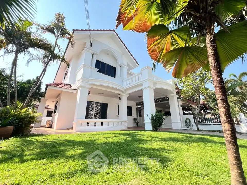 Stunning white two-story house with lush green lawn and tropical palm trees.