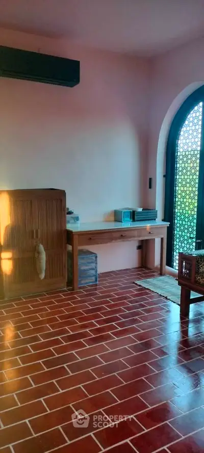 Charming interior with rustic brick flooring and elegant arched window, perfect for cozy living.