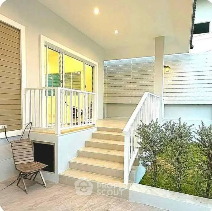 Charming modern home entrance with steps leading to a cozy patio, surrounded by lush greenery.
