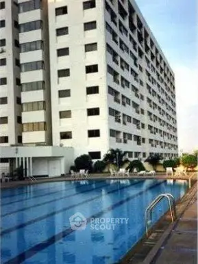 Modern apartment building with a large swimming pool and sunlit exterior.