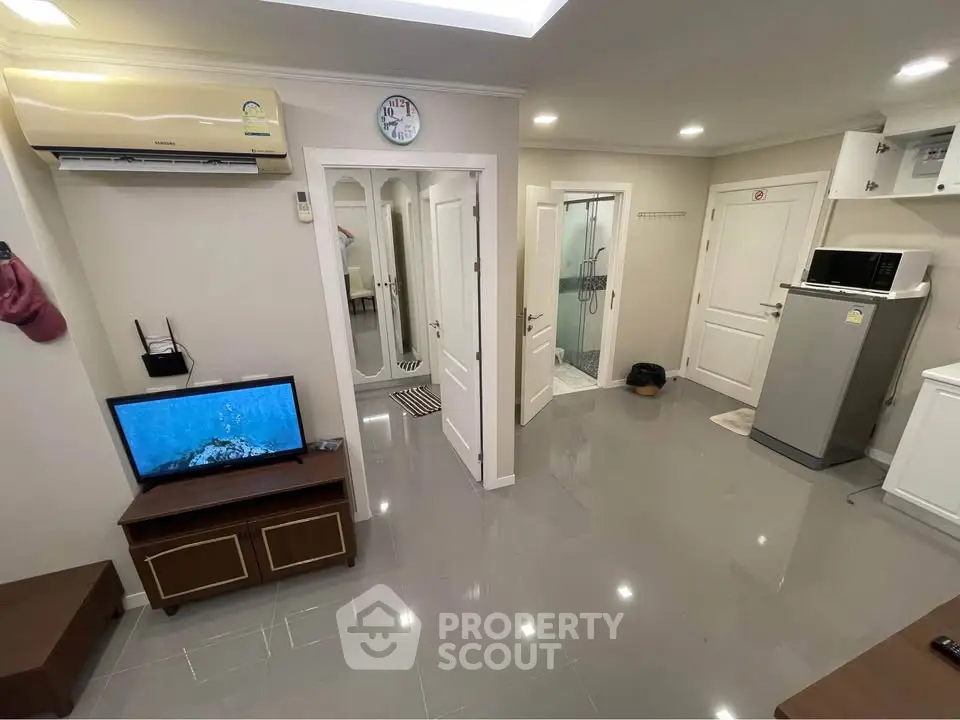 Modern living room with sleek flooring, air conditioning, and a compact kitchen area.