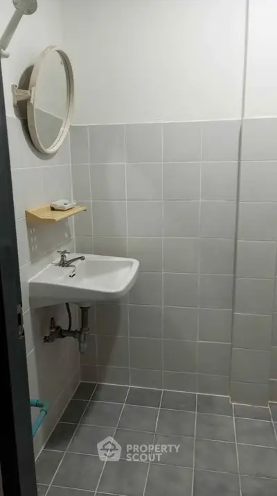 Compact bathroom with wall-mounted sink and round mirror, featuring minimalist design and neutral tiles.